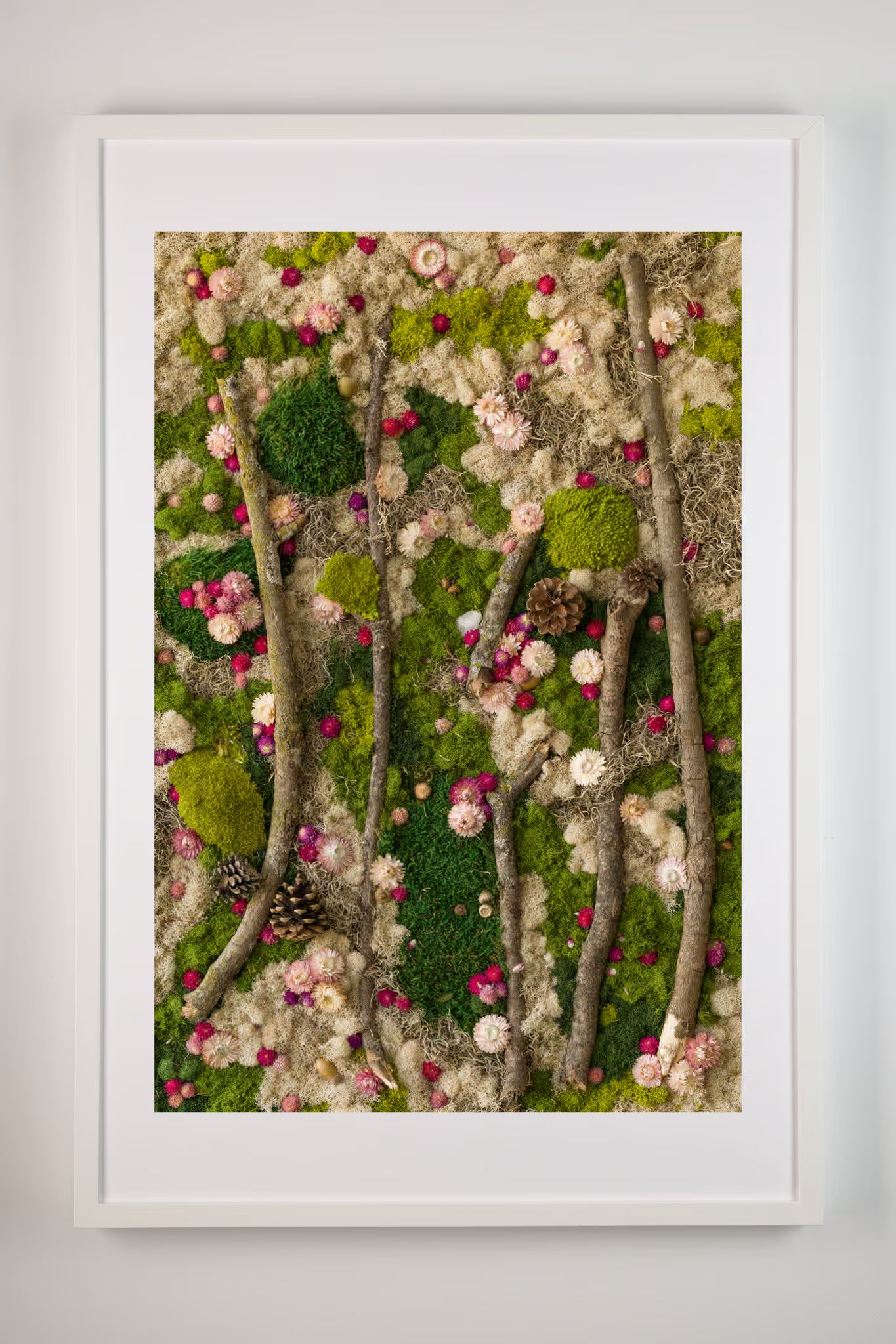 Framed fine art print of a forest scene with green moss foliage and pink flowers on a white wall.