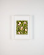 Framed artwork of pink flowers on green moss against a white wall